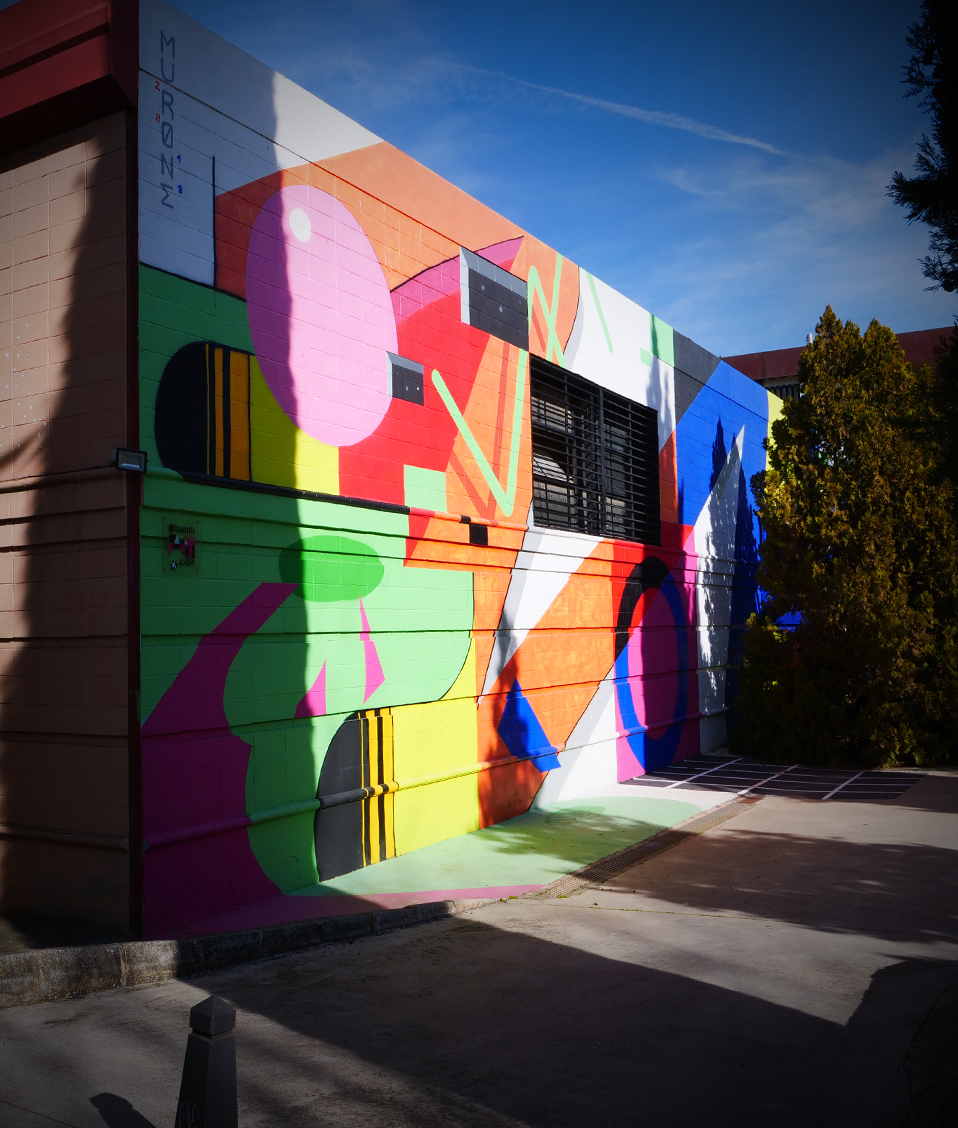 Exterior de una instalación de la Facultad de Bellas Artes con la pared llena de dibujos coloridos y con árboles alrededor